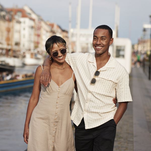 Happy young man with hand in pocket walking arm around of woman on pier