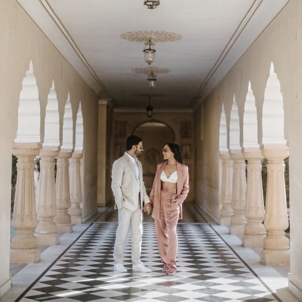bride and groom wearing suits for pre-wedding photos; bride wearing a pink suit and groom wearing a grey suit