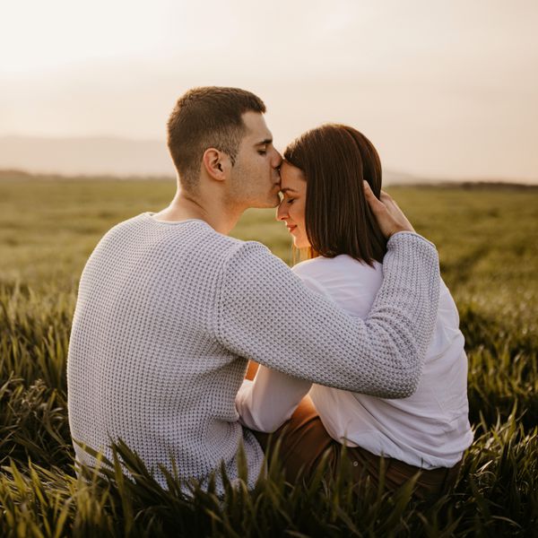 Couple sitting on grass while the man kisses the forehead of the woman
