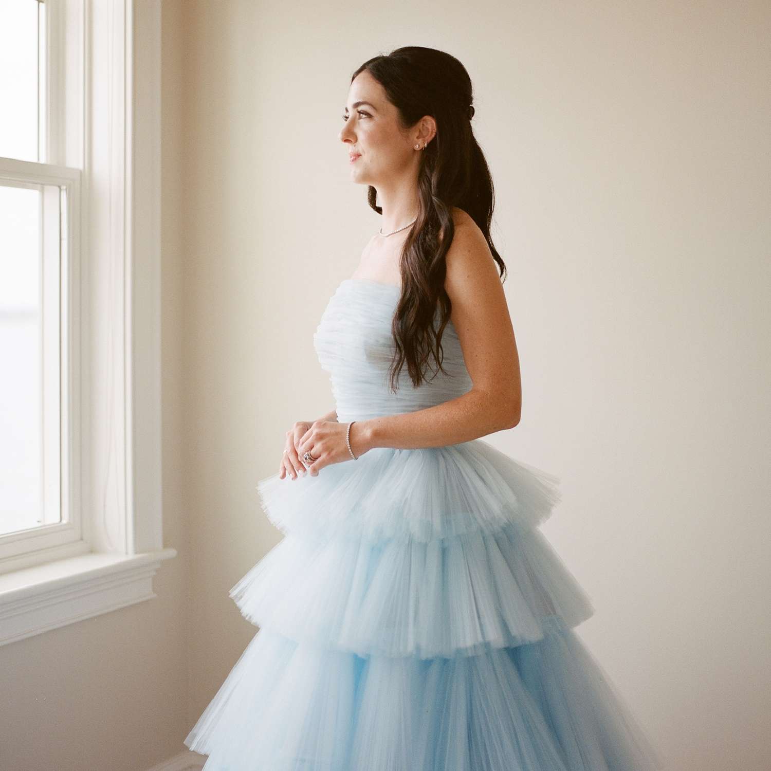 bride wearing a blue tulle wedding dress looking out the window