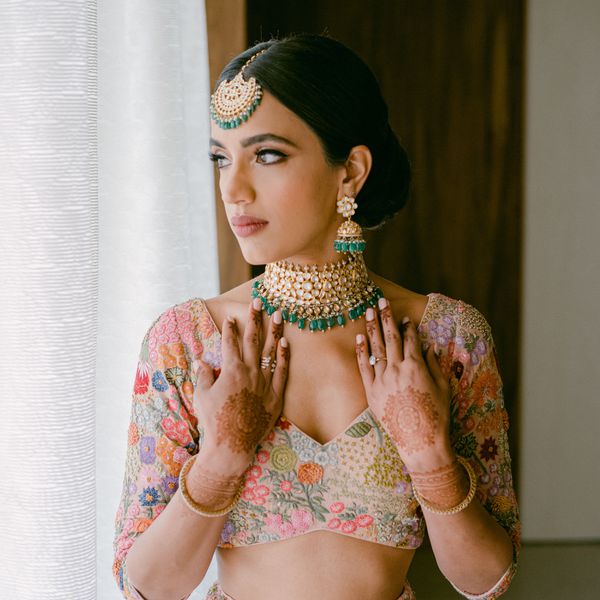 bride wearing a colorful, floral lehenga with gold jewelry