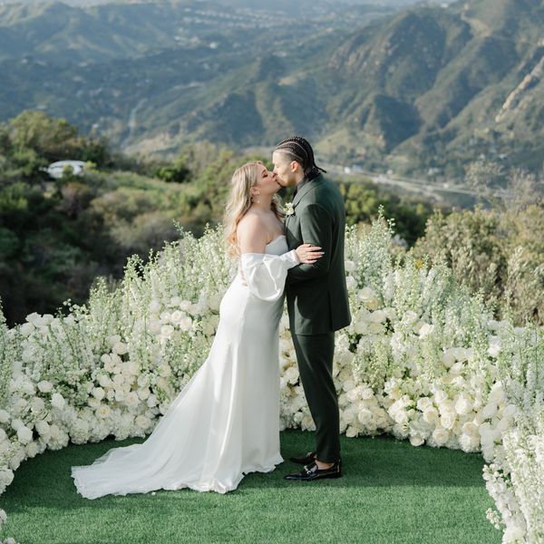 bride and groom kissing amongst a mountainous backdrop with white flowers surrounding them