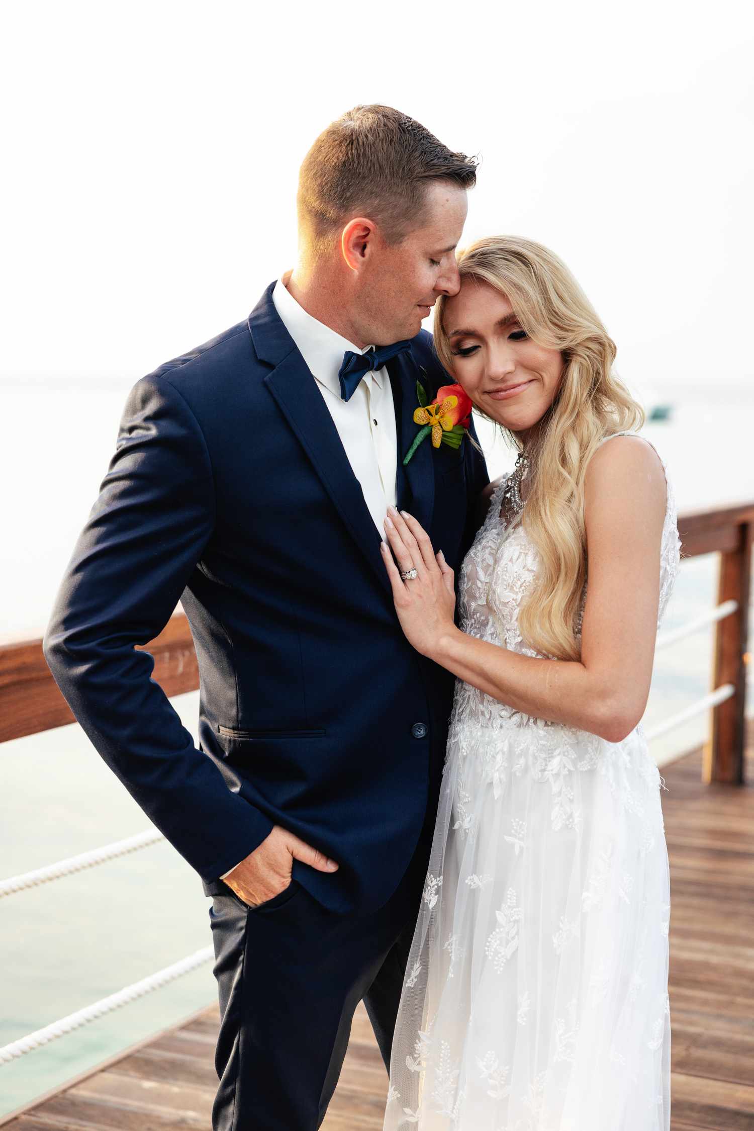 Bride in White Wedding Dress With Hair Down Posing with Groom in Navy Tuxedo by The Ocean