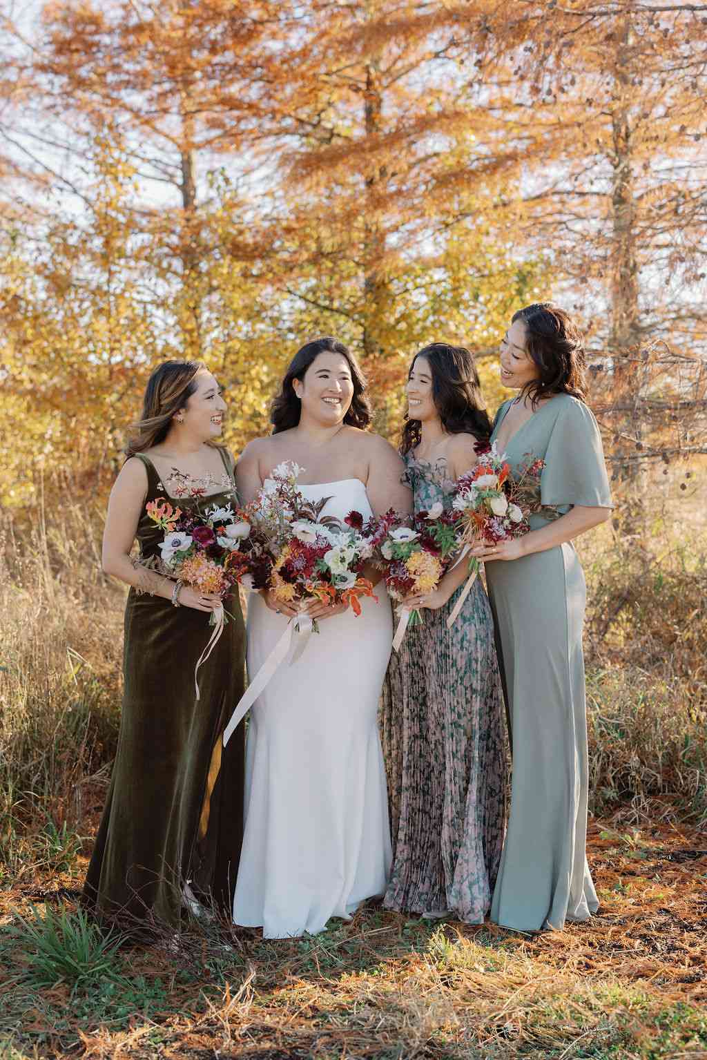 Bride in Strapless Wedding Dress Holding Colorful Bouquet Posing With Bridesmaids in Various Shades of Green Dresses