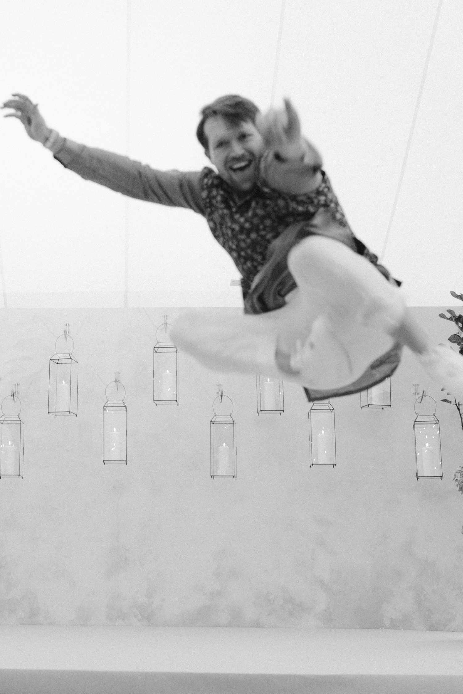 Black and white portrait of groom in floral kurta and white pants dancing in front of laterns