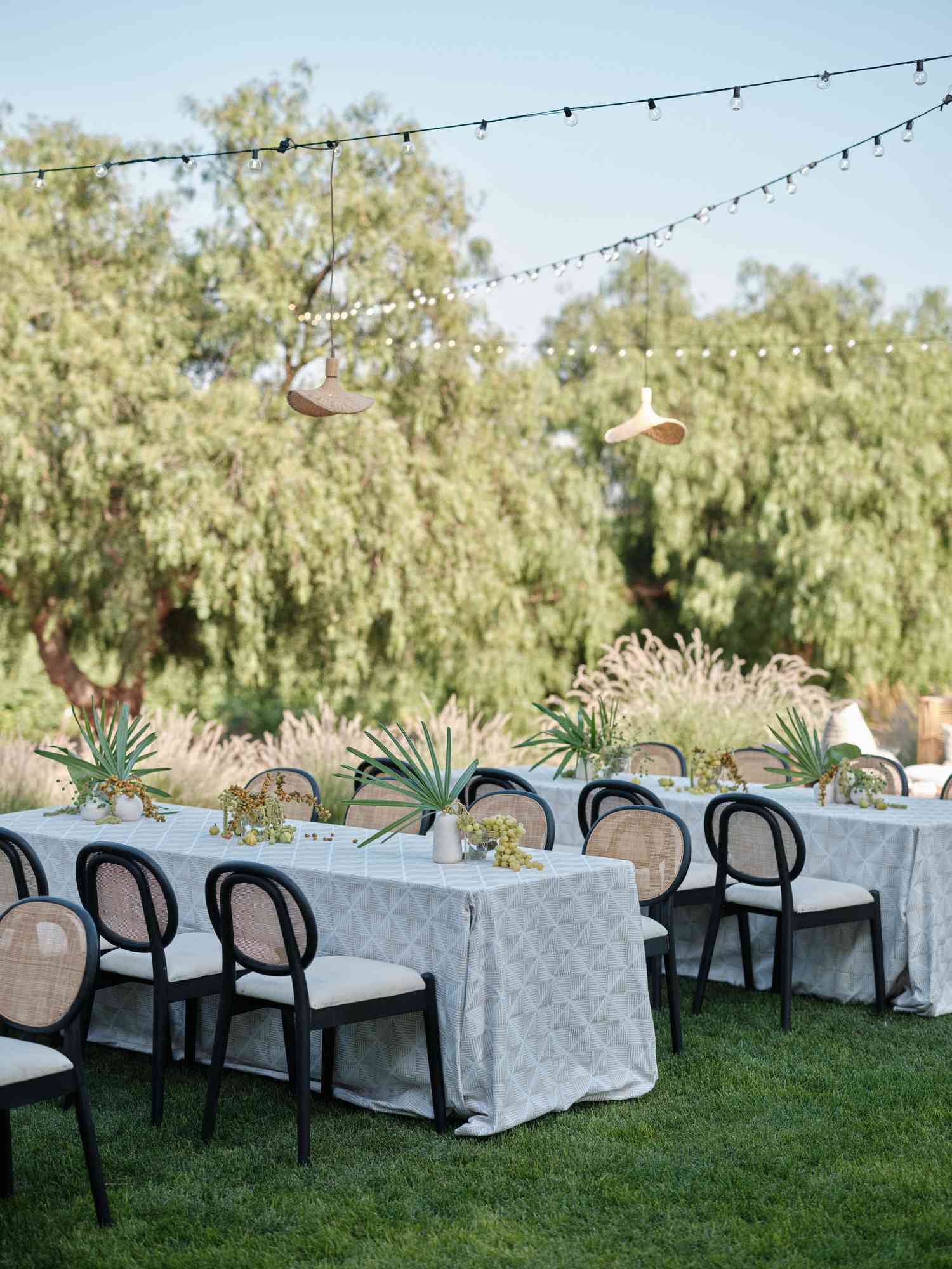 Small White Tables With Black and White Chairs and Plant Decor and String Lights Above