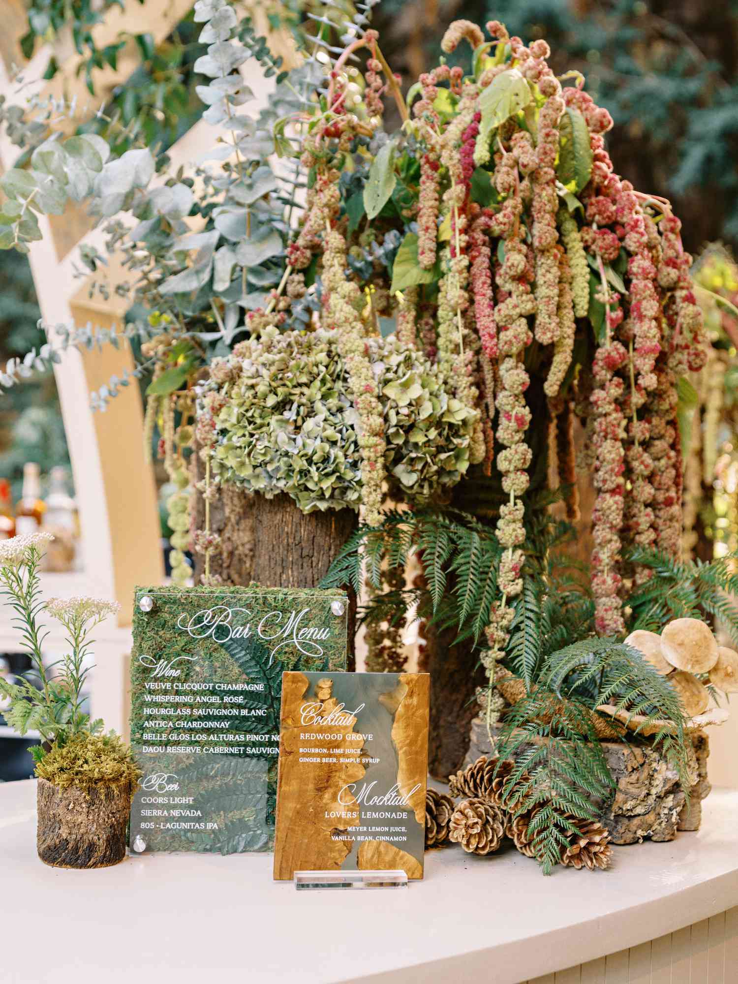 Cocktail Menu on Pressed Leaves In Front of Fern, Pine Cone, and Flower Decor on Tree Strump