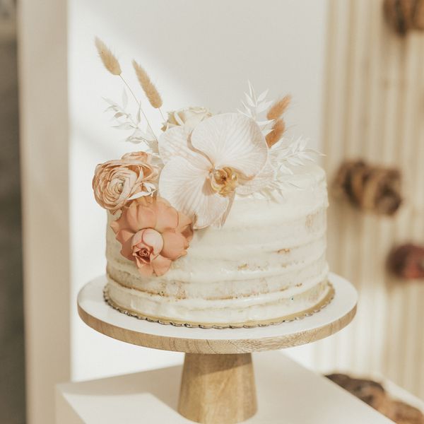 A small wedding cake with white icing and white and pink fresh flowers.