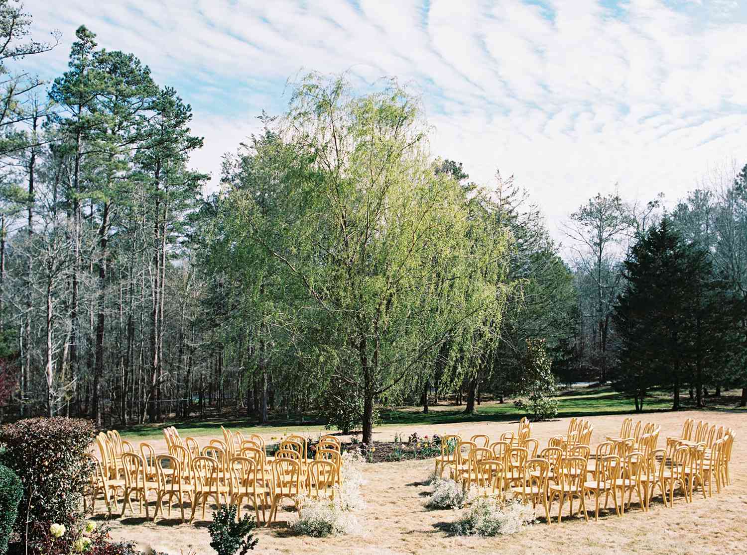 Wooden Chairs at Outdoor Wedding Ceremony With White Flowers Along Aisle