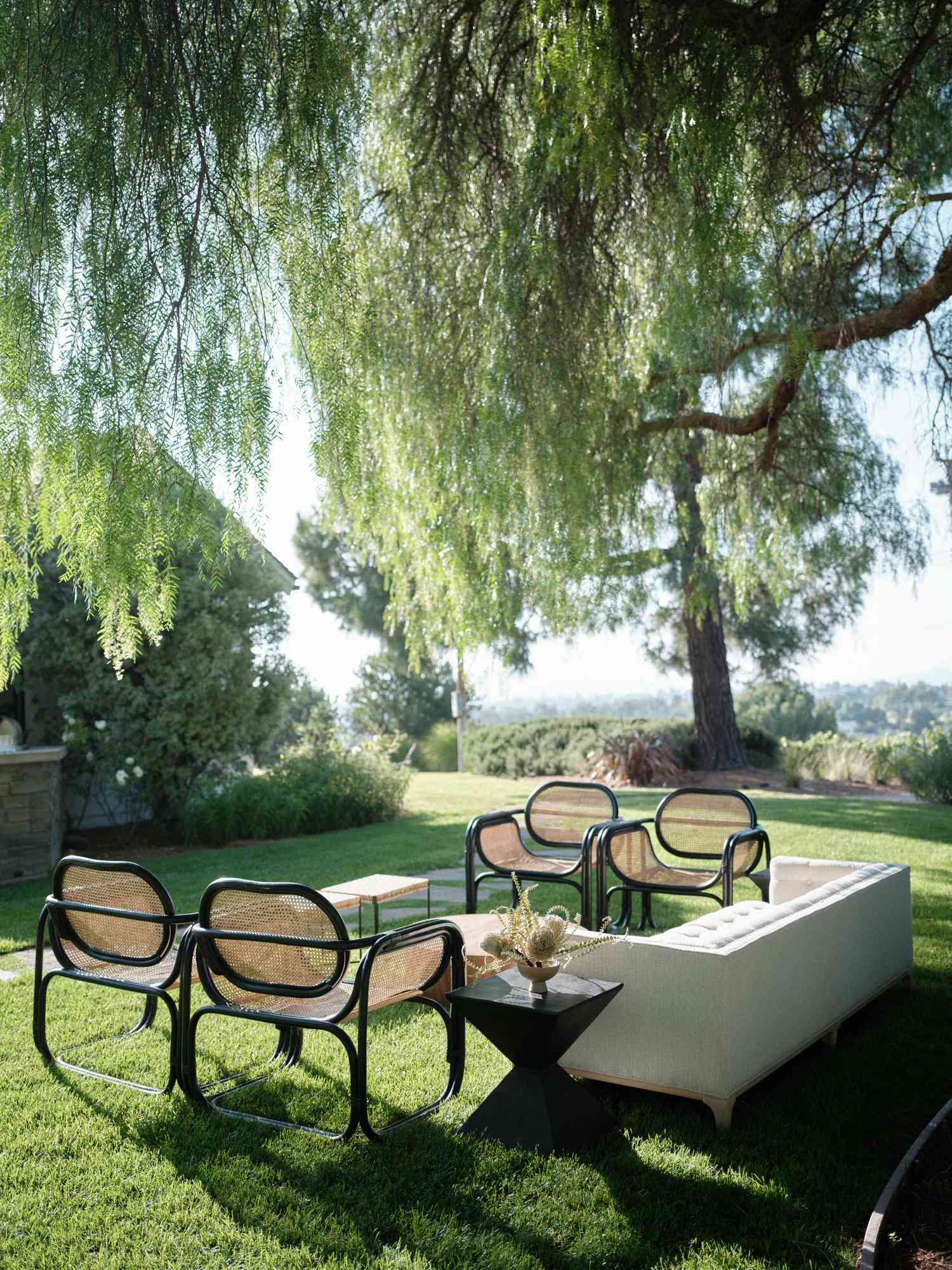 Lounge Area with White Couch and Rattan Chairs Under Willow Tree
