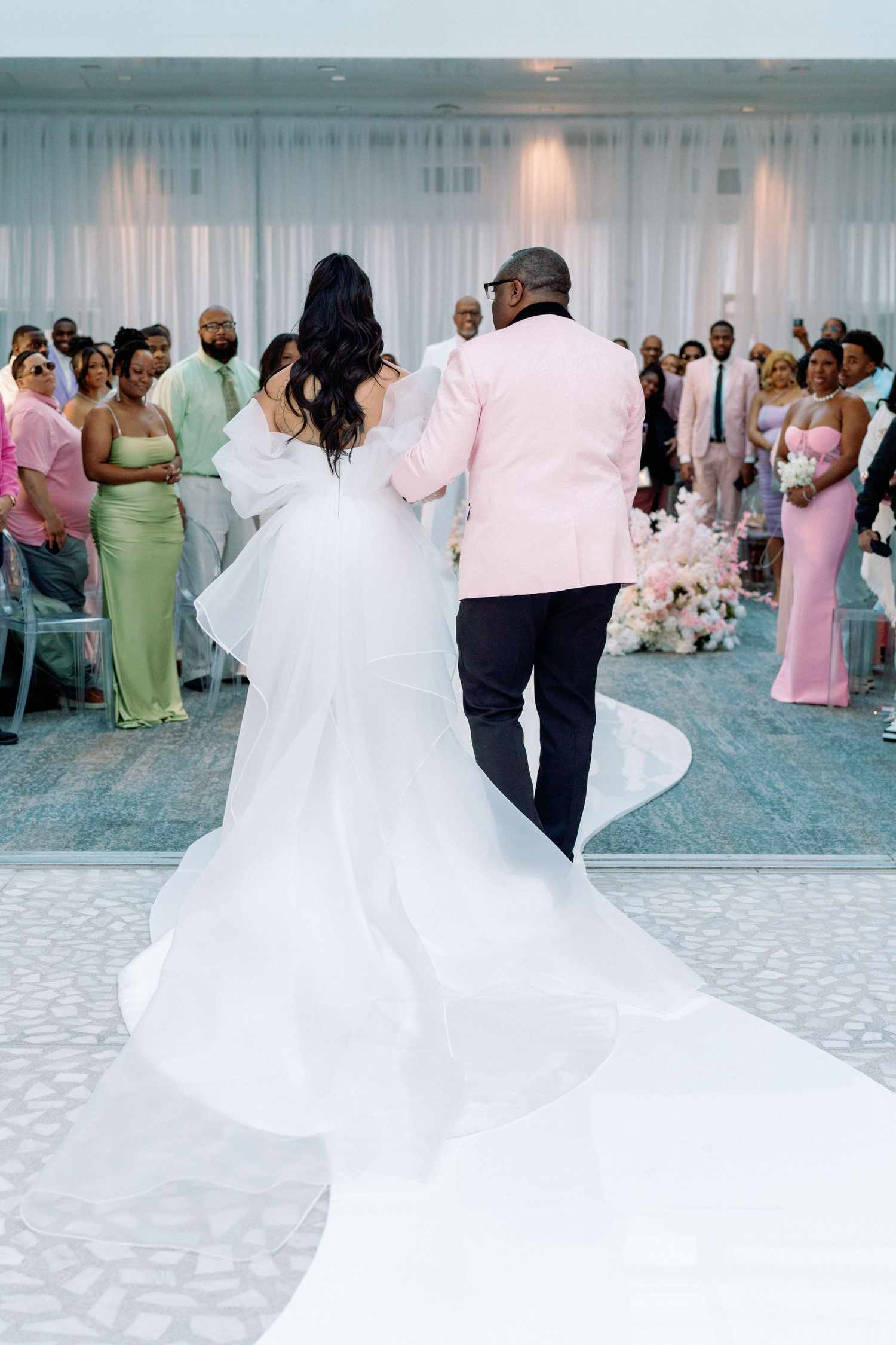 bride in white dress and father in pink suit jacket facing with backs turned
