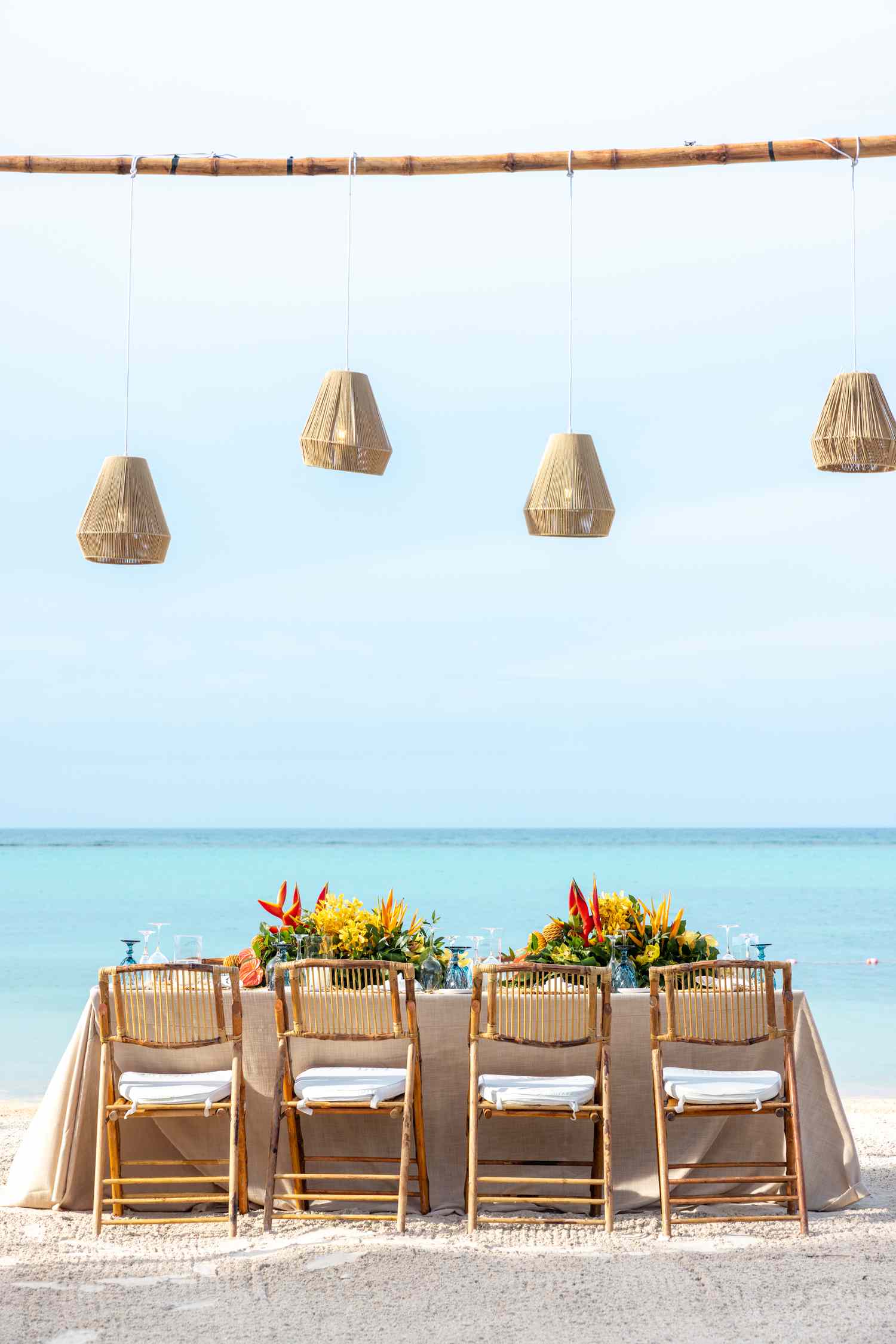 Small Reception Table With Colorful Flower Decor and Hanging Lamp Fixtures On the Beach