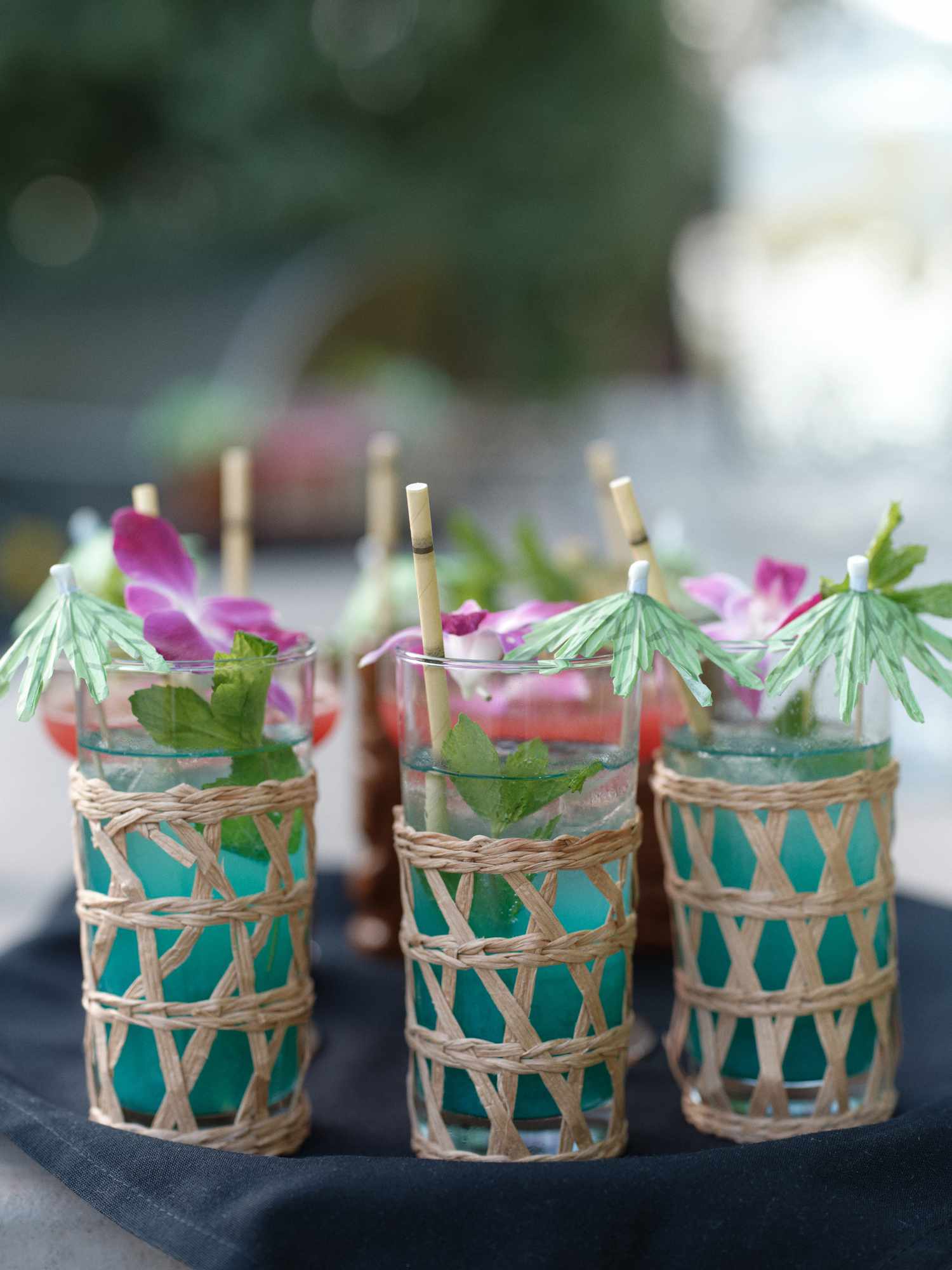 Close Up of Blue Cocktails With Twigs Wrapped Around Glass and Green Umbrellas