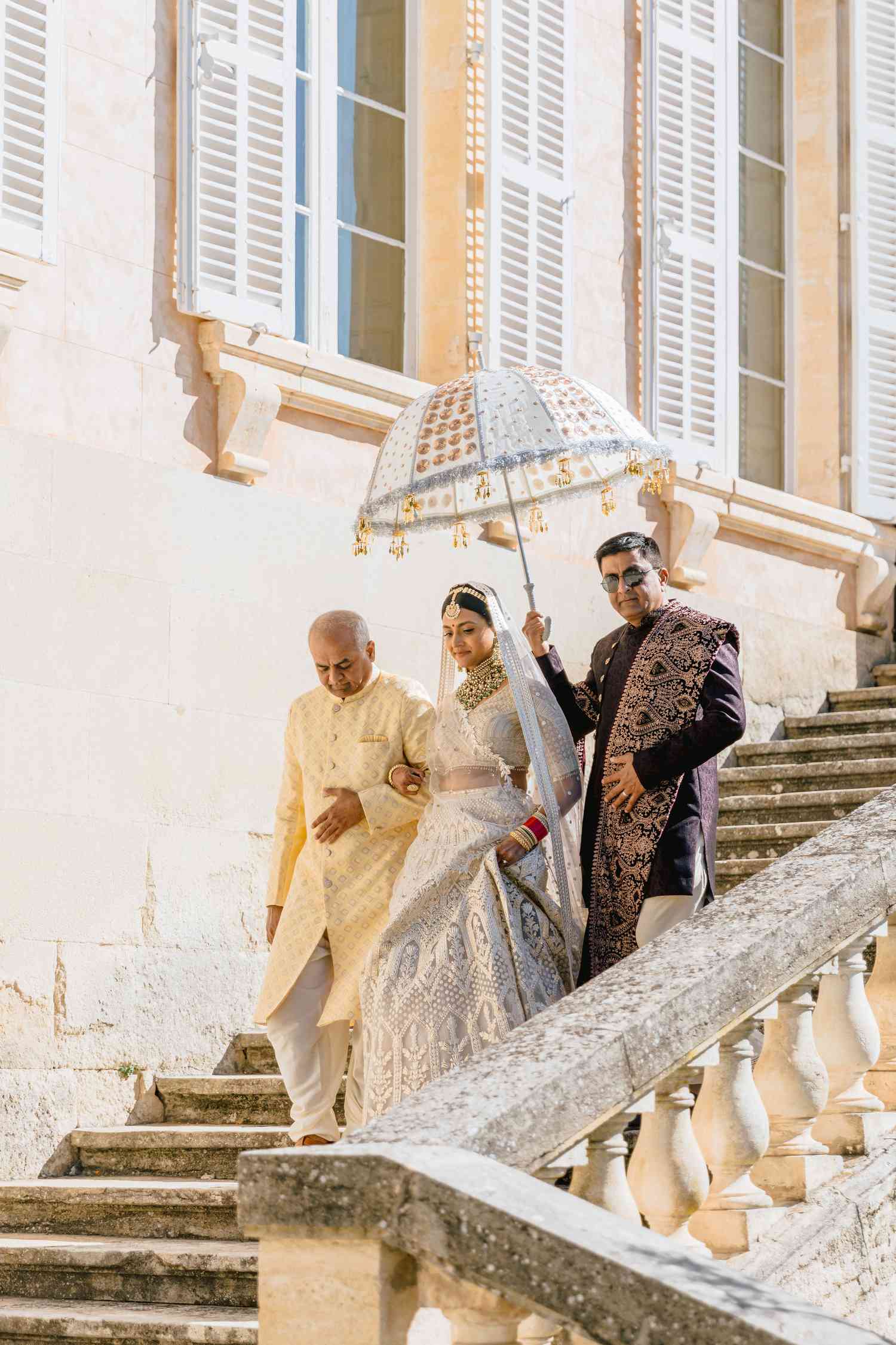 bride in traditional Indian wedding attire walking down stairs with parents