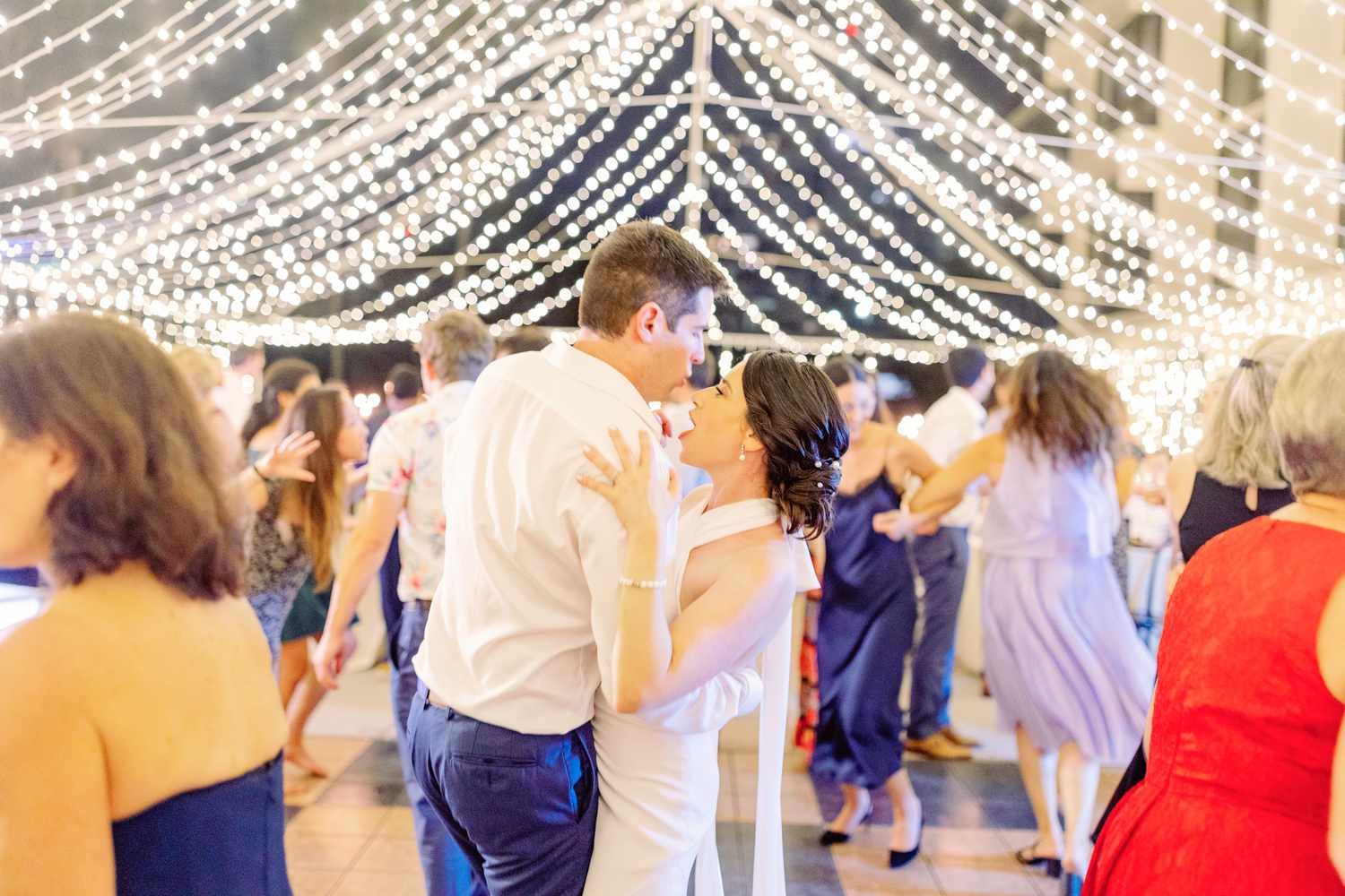 Bride in Halter Top Wedding Dress Dancing with Groom in Blue Suit Under String Lights