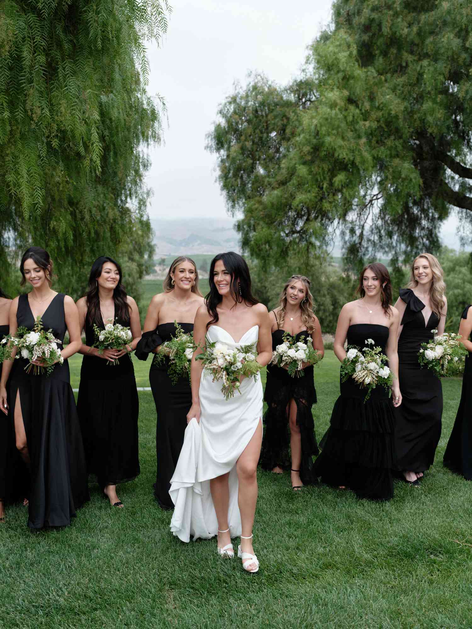 Bride in White Wedding Dress and Hair Down Holding White Bouquet Posing With Bridesmaids in Black Dresses