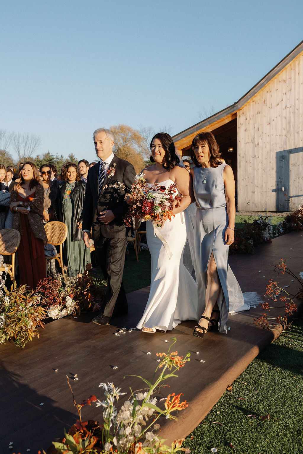 Bride in Strapless Wedding Dress Walking Down Aisle With Mother in Gray Dress and Father in Black Suit