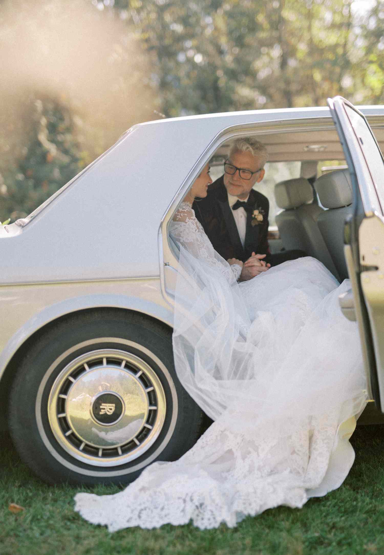 Bride in Lace Wedding Dress In Classic Car With Father in Black Tuxedo