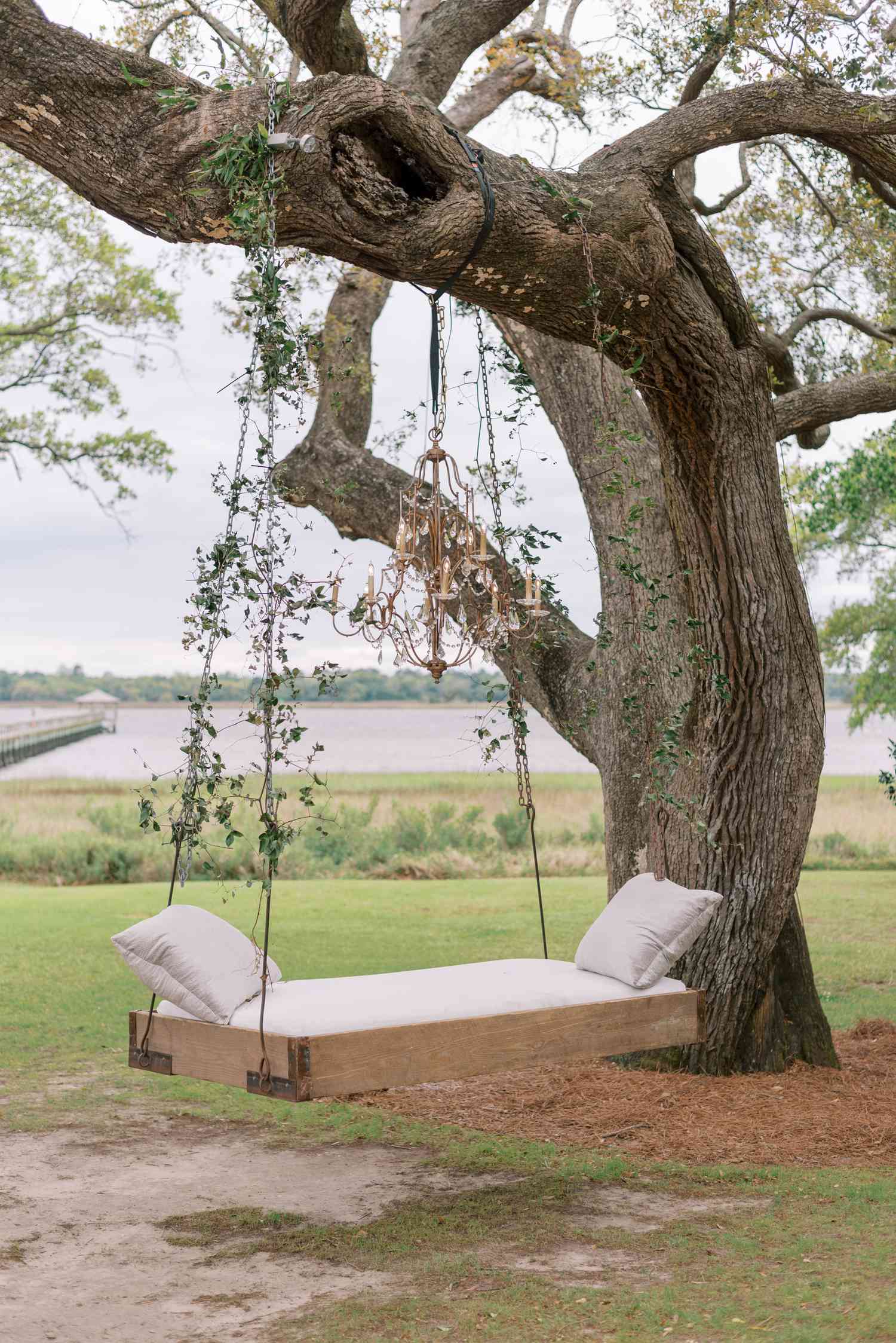 Sofa swing tied to large tree with chandelier overlooking rustic landscape