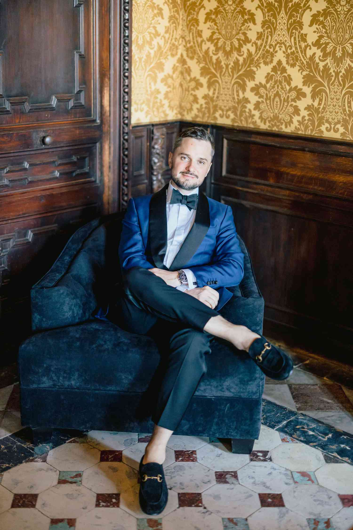 groom sitting in velvet chair in navy and black suit