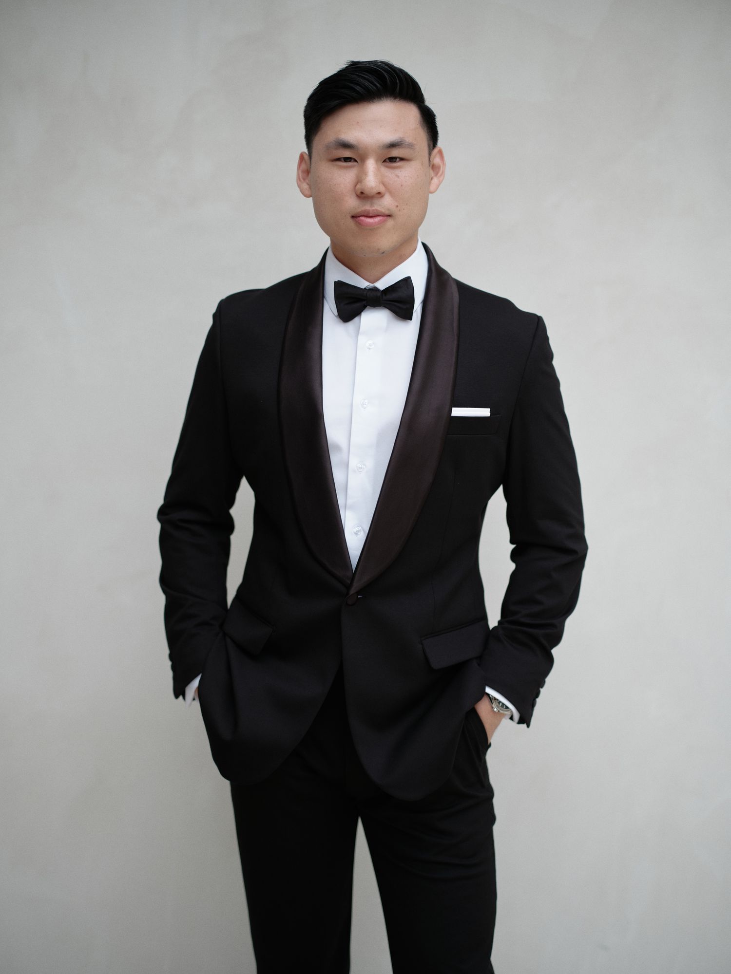 Portrait of Groom in Black Tuxedo in Front of White Wall