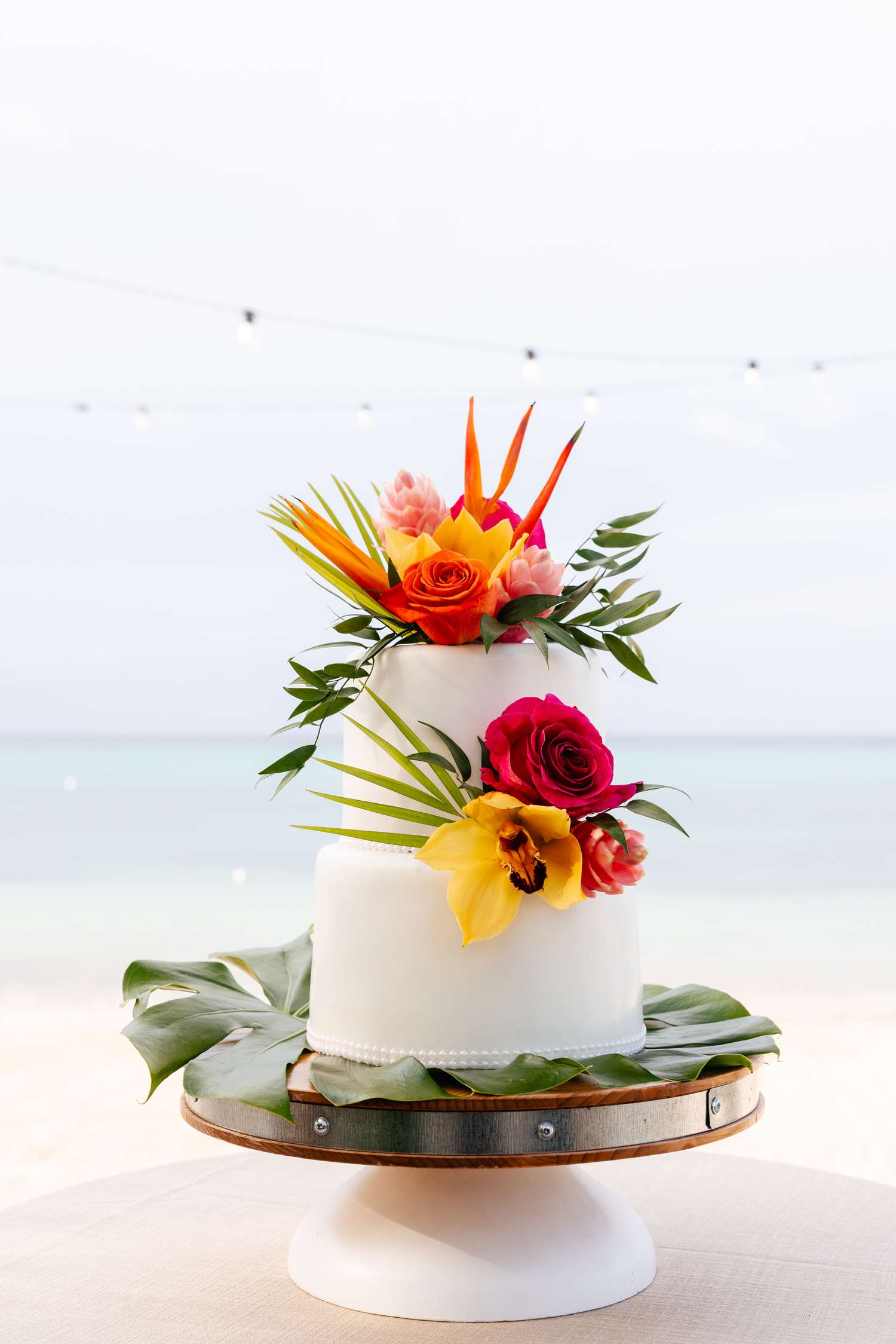Two Tier White Wedding Cake With Tropical Flowers With Ocean in Background