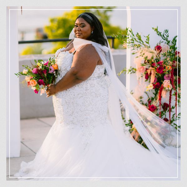 a bride wearing a crystal-embellished mermaid wedding dress holding a wedding bouquet of peach, red, and pink flowers
