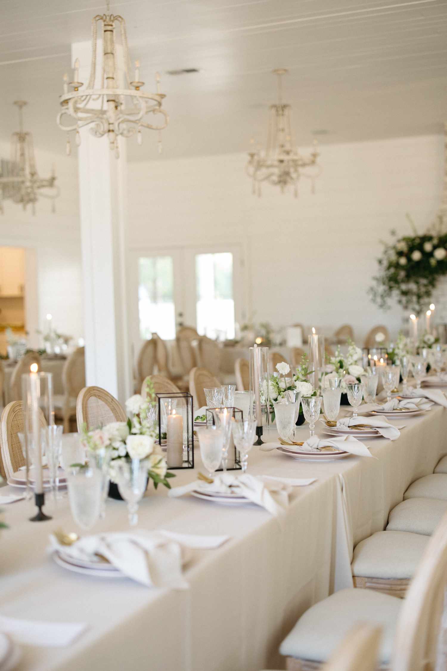 Beige Reception Tables With White Flower Decor, Candles, and Chandeliers Above