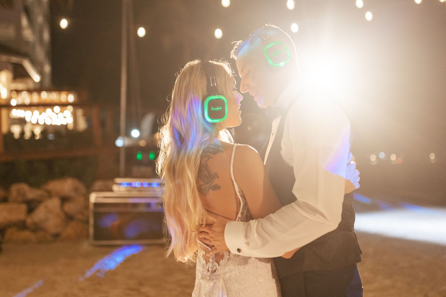 Bride in Wedding Dress With Hair Down Dancing With Groom in Tuxedo With Headphones on Beach