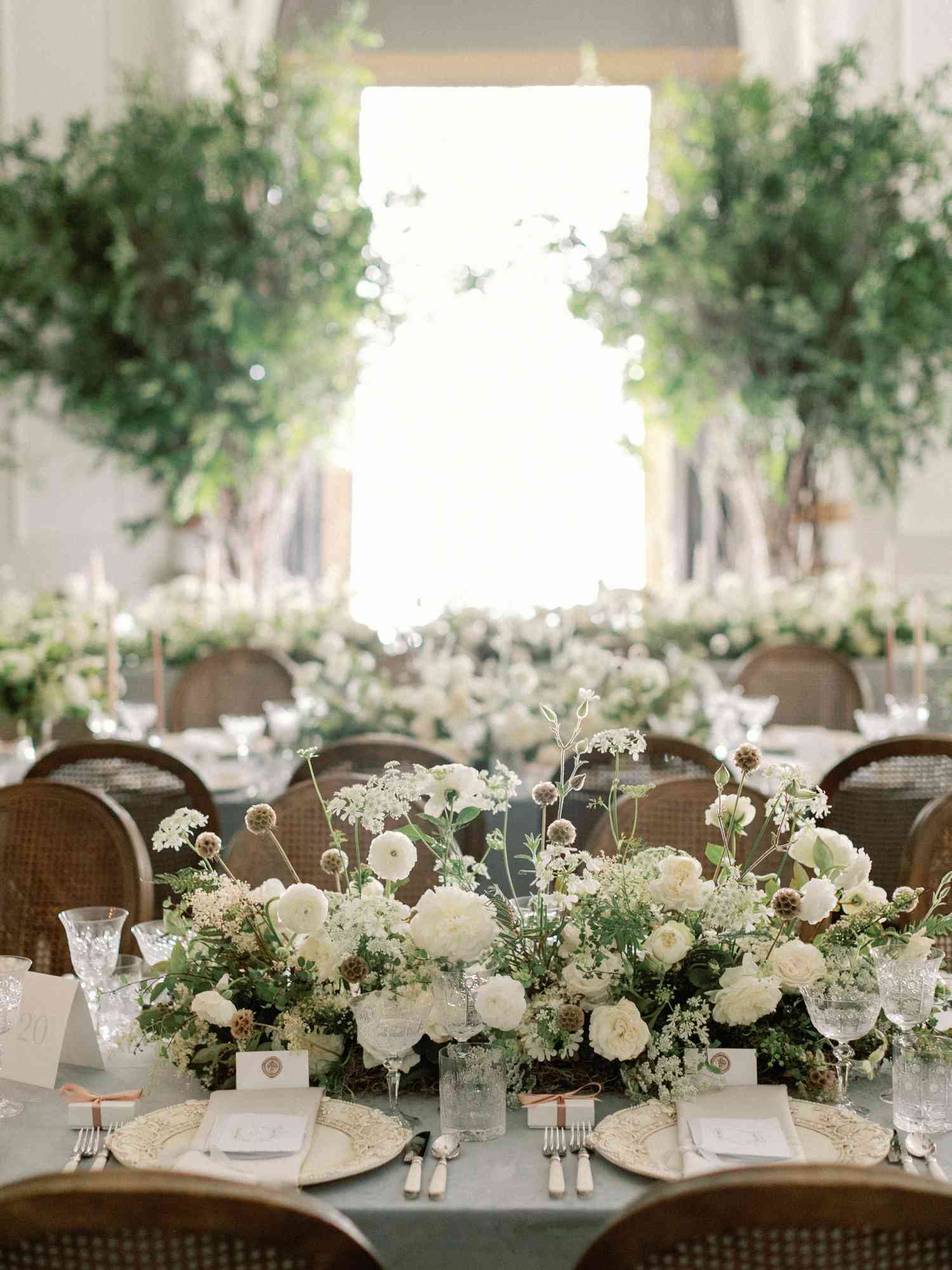Wedding Reception Table With Low Floral Centerpiece of White Roses, Ranunculus, Queen Anne's Lace, and Greenery