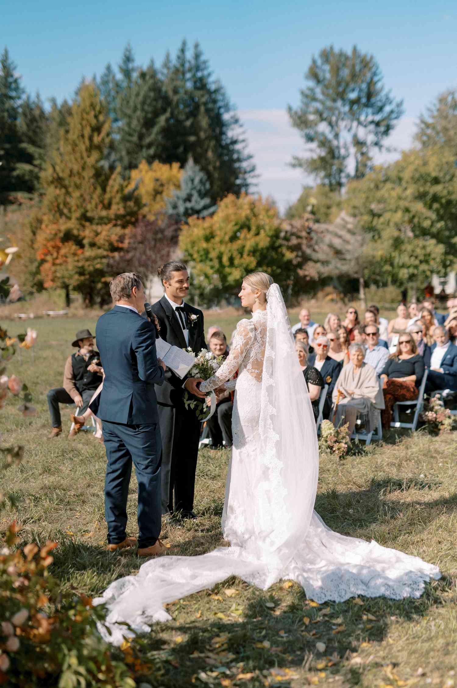 Bride in Lace Wedding Dress With Long Veil At Altar With Groom in Black Tuxedo