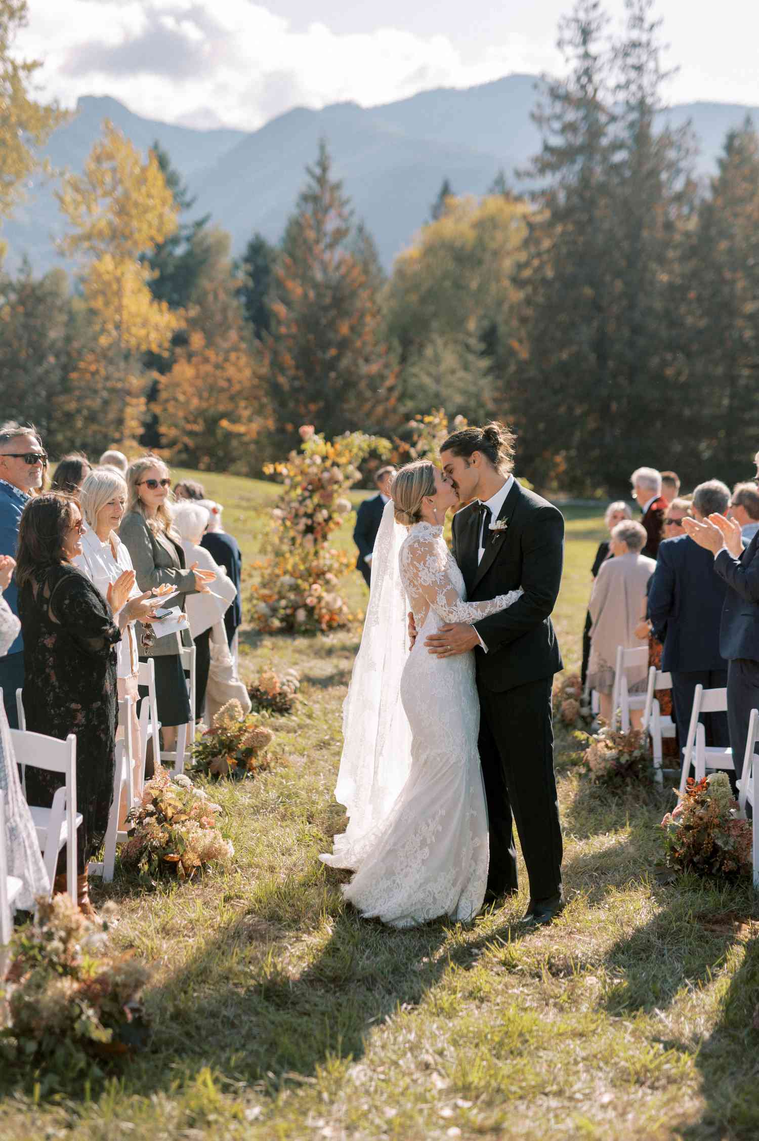 Bride In Lace Wedding Dress And Long Veil Kissing Groom in Black Tuxedo in Aisle