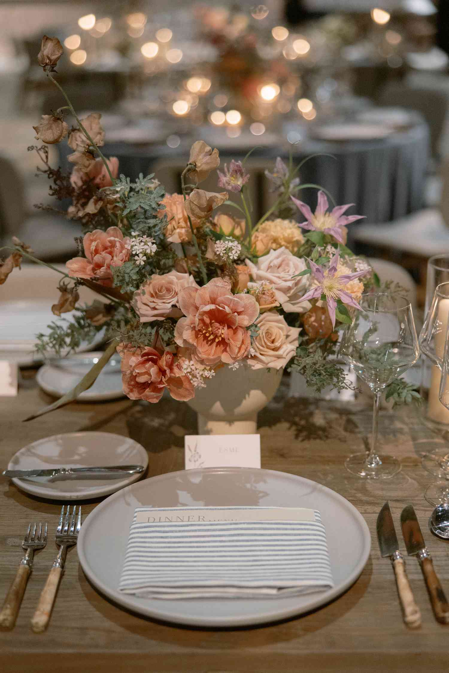 wedding centerpiece with peach, pink, and purple flowers in front of place setting with striped napkin
