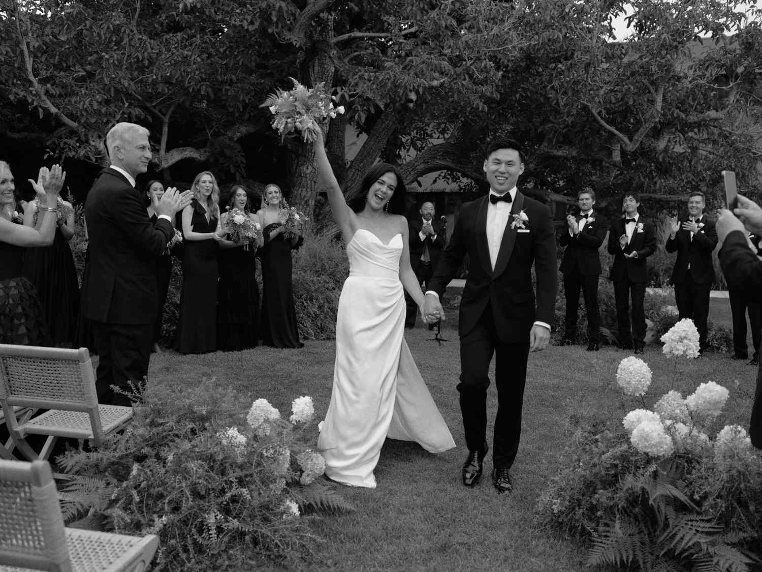 Bride in Wedding Dress Holding Bouquet Holding Hands With Groom in Tuxedo After Wedding Ceremony