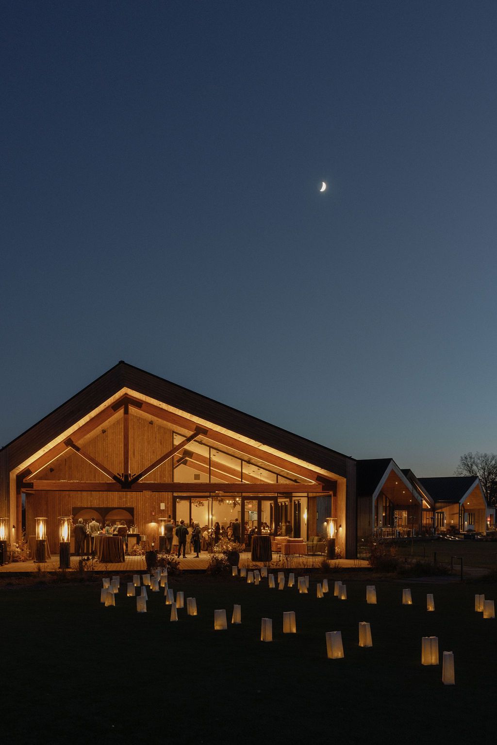 Wooden Reception Venue Illuminated at Night With White Lanterns Out Front
