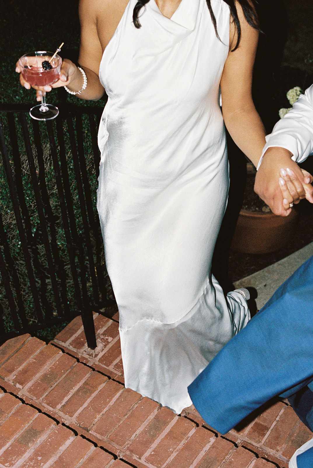 Close Up of Bride in White Silk Dress Holding Cocktail Walking Up Brick Staircase