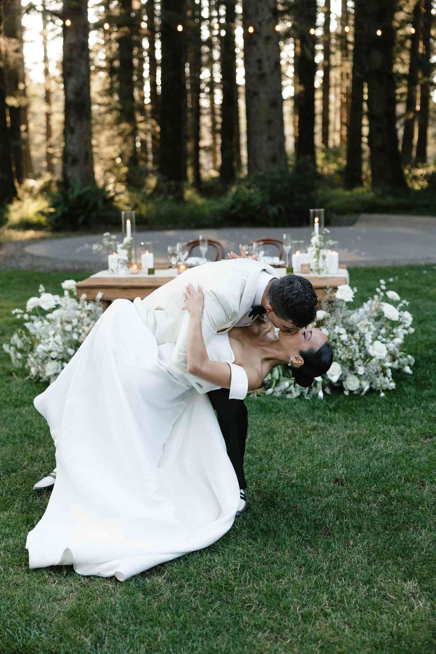 Koko lwasaki in White Off the Shoulder Wedding Dress and Veil and Kiki Nyemchek in White Tuxedo With Black Bow Tie Kissing After First Dance in Front of Sweetheart Table
