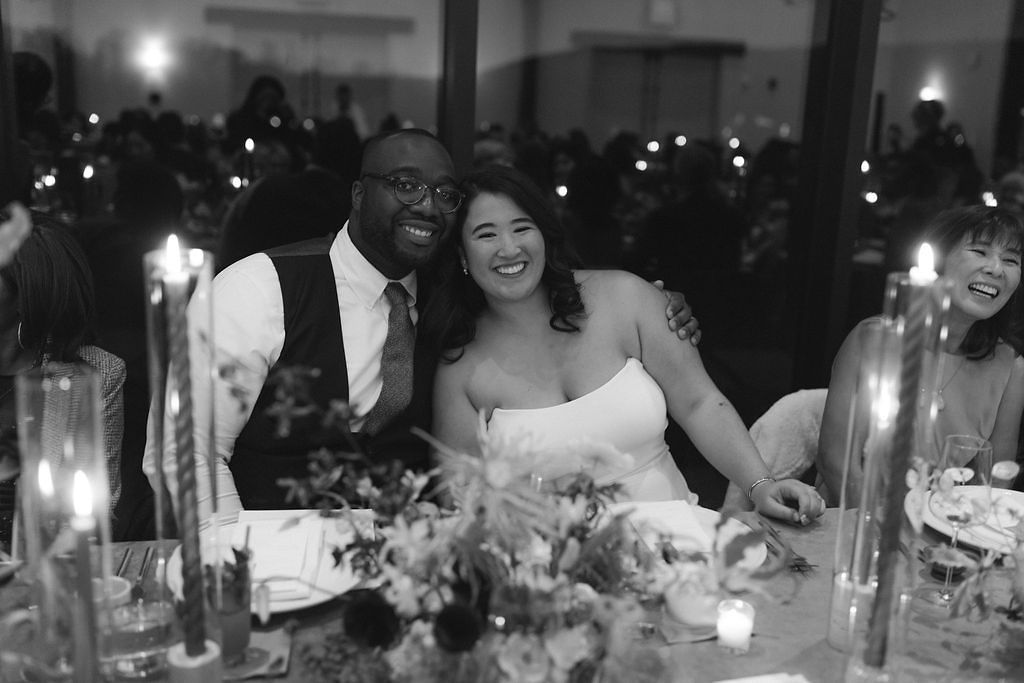 Black and White Image of Bride in Strapless Dress Posing With Groom in Tuxedo at Reception Table