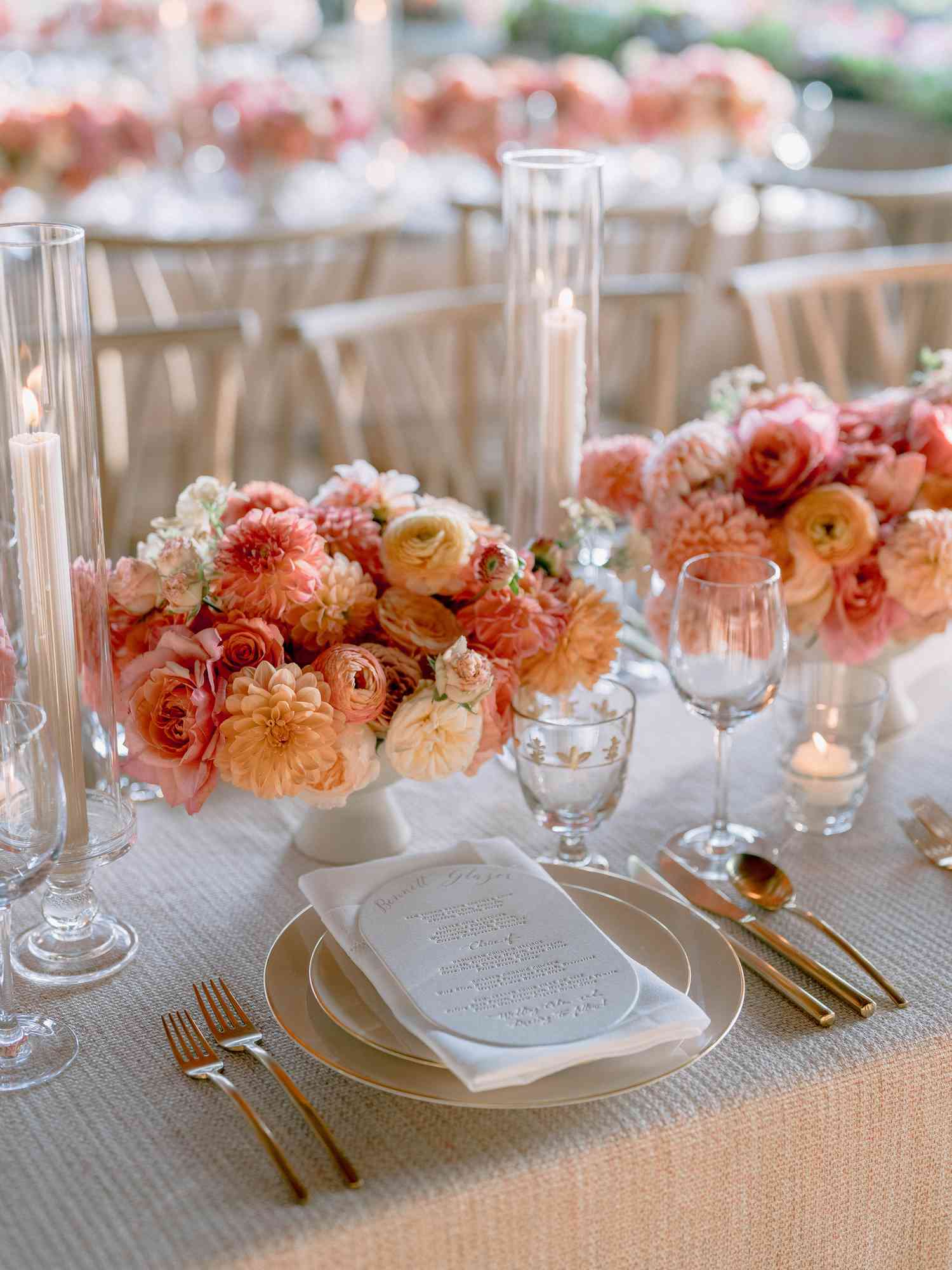 dining table with white table cloth and pink flower center pieces and table setting with a menu on a plate