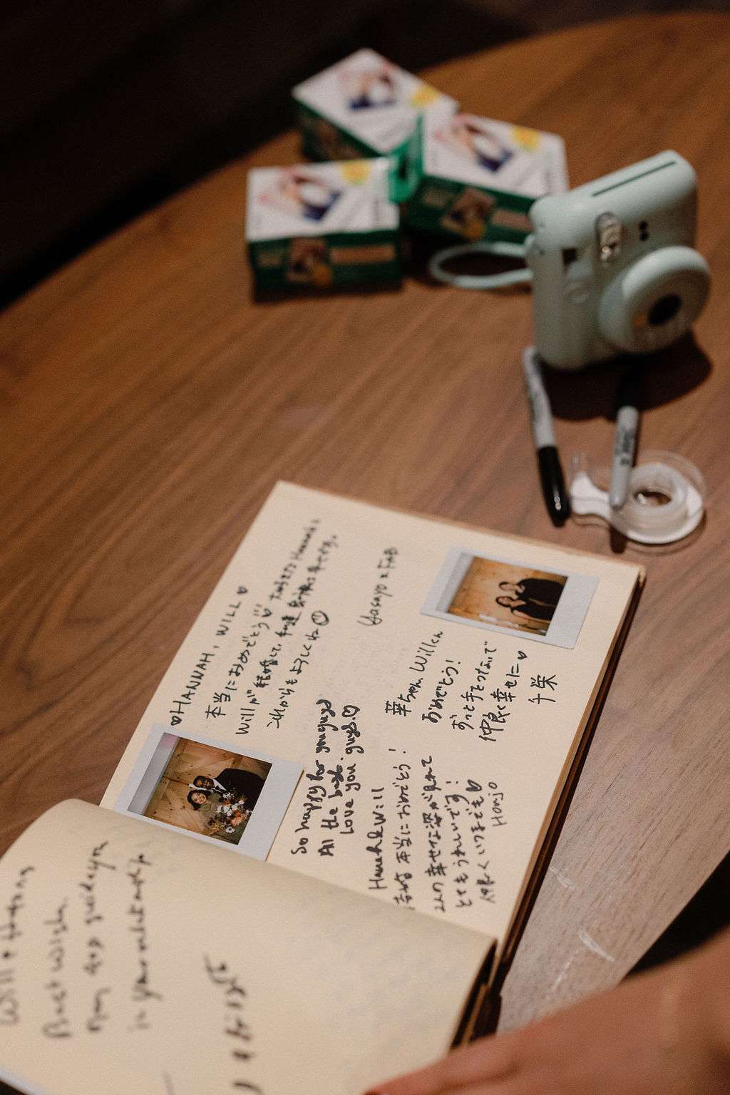 Wedding Guest Book Next to Polaroid Camera on Wooden Table at Wedding Reception