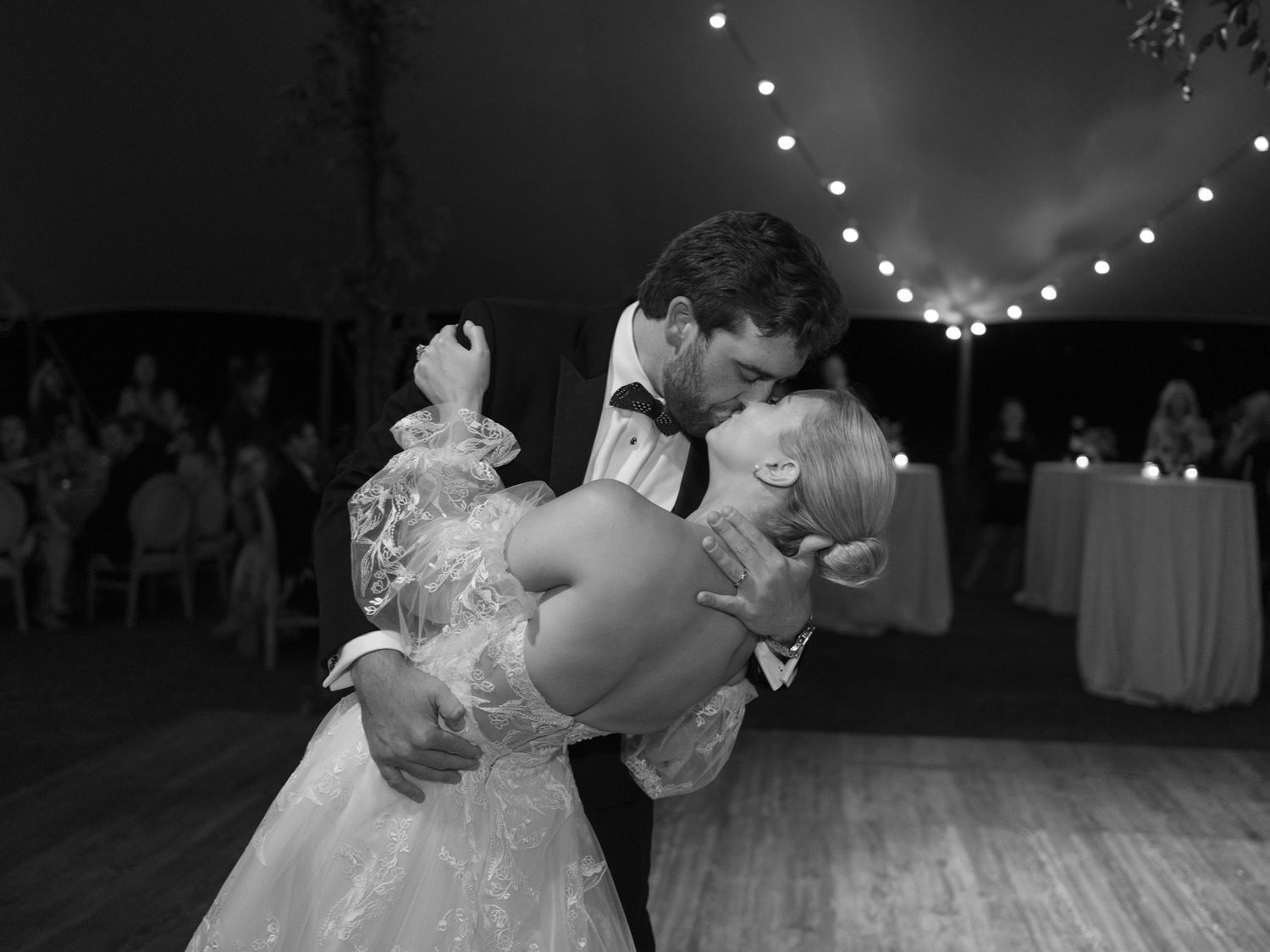 Black and White Portrait of Bride in Lace Dress Kissing Groom in Tuxedo at Reception