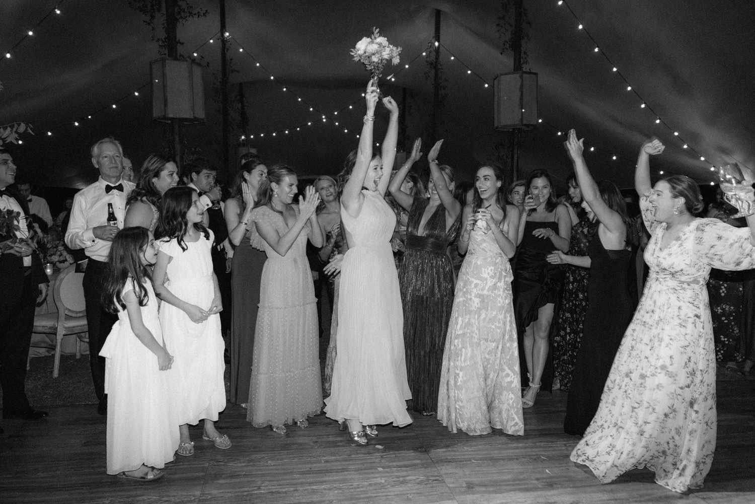 Black and White Image of Bridesmaids in Floral Dresses Catching Bouquet at Reception