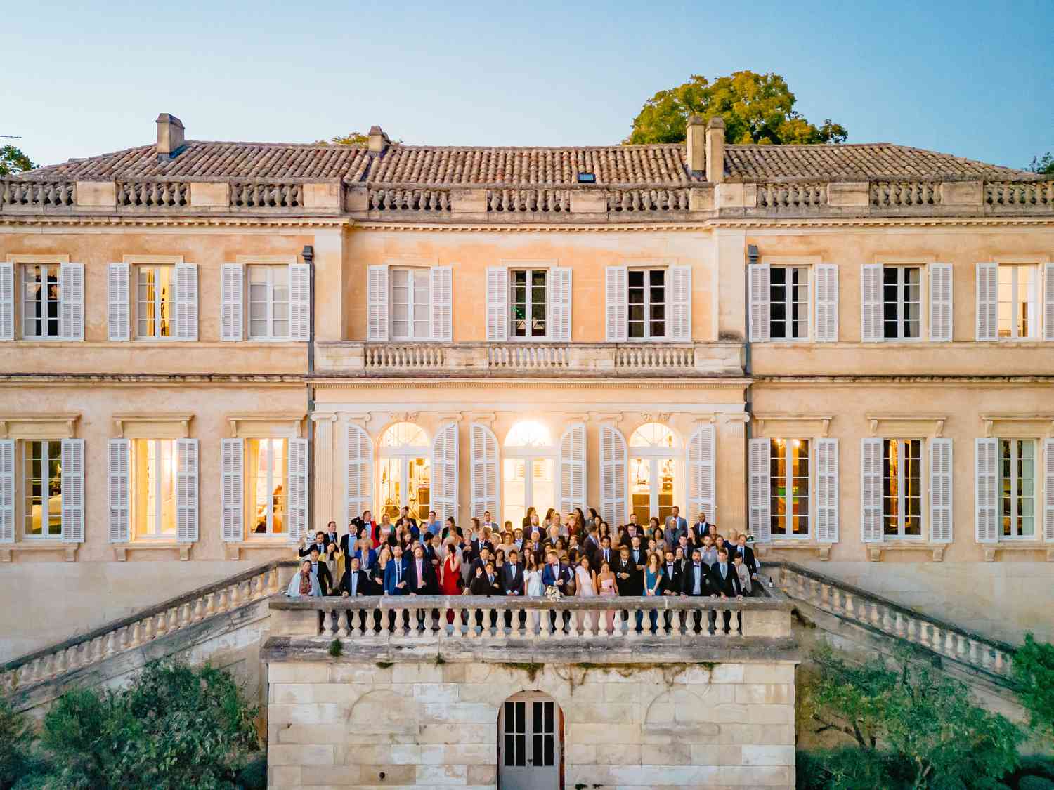 group photo of guests and bride and groom in front of tan mansion