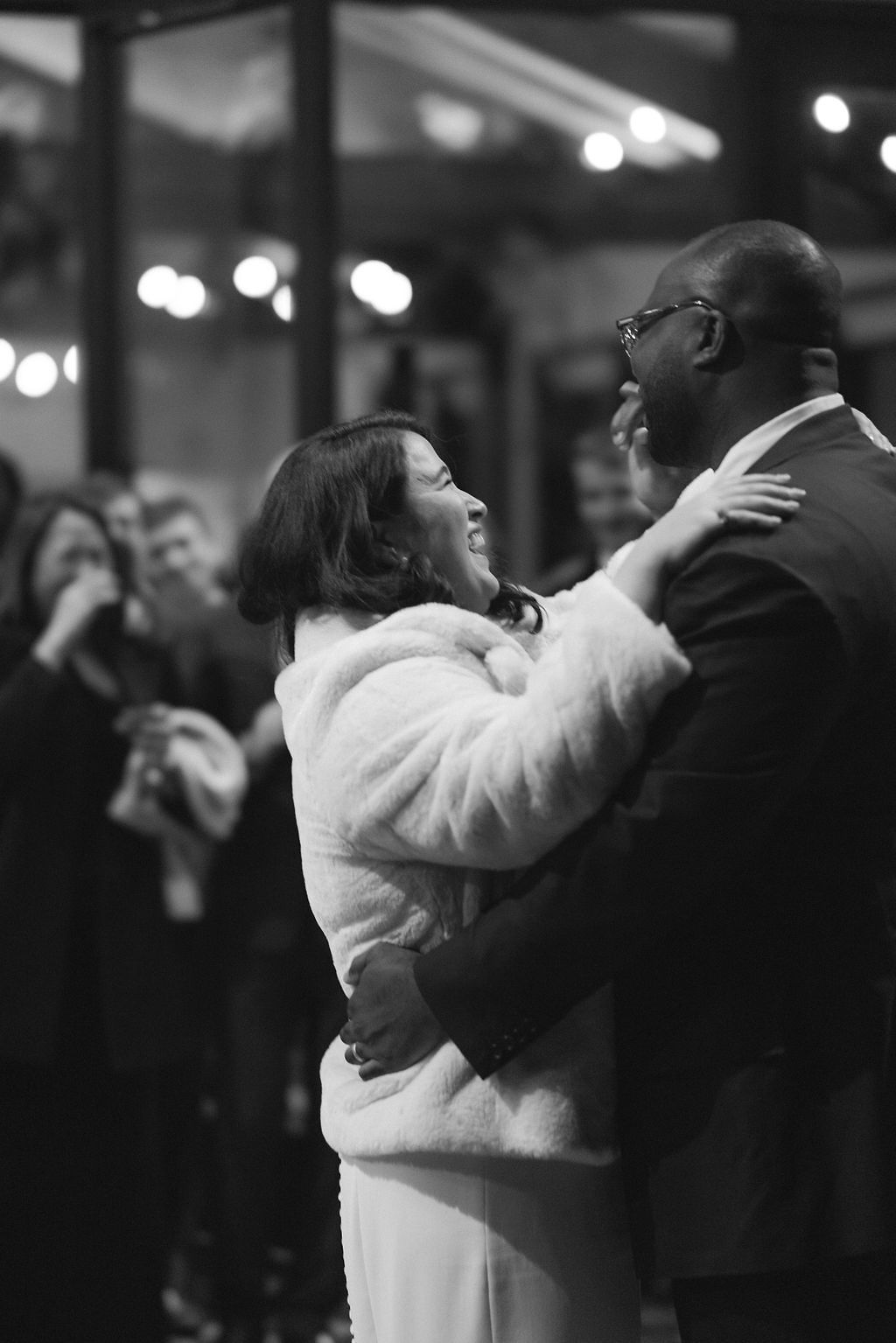 Black and White Image of Bride in Coat Dancing With Groom in Tuxedo