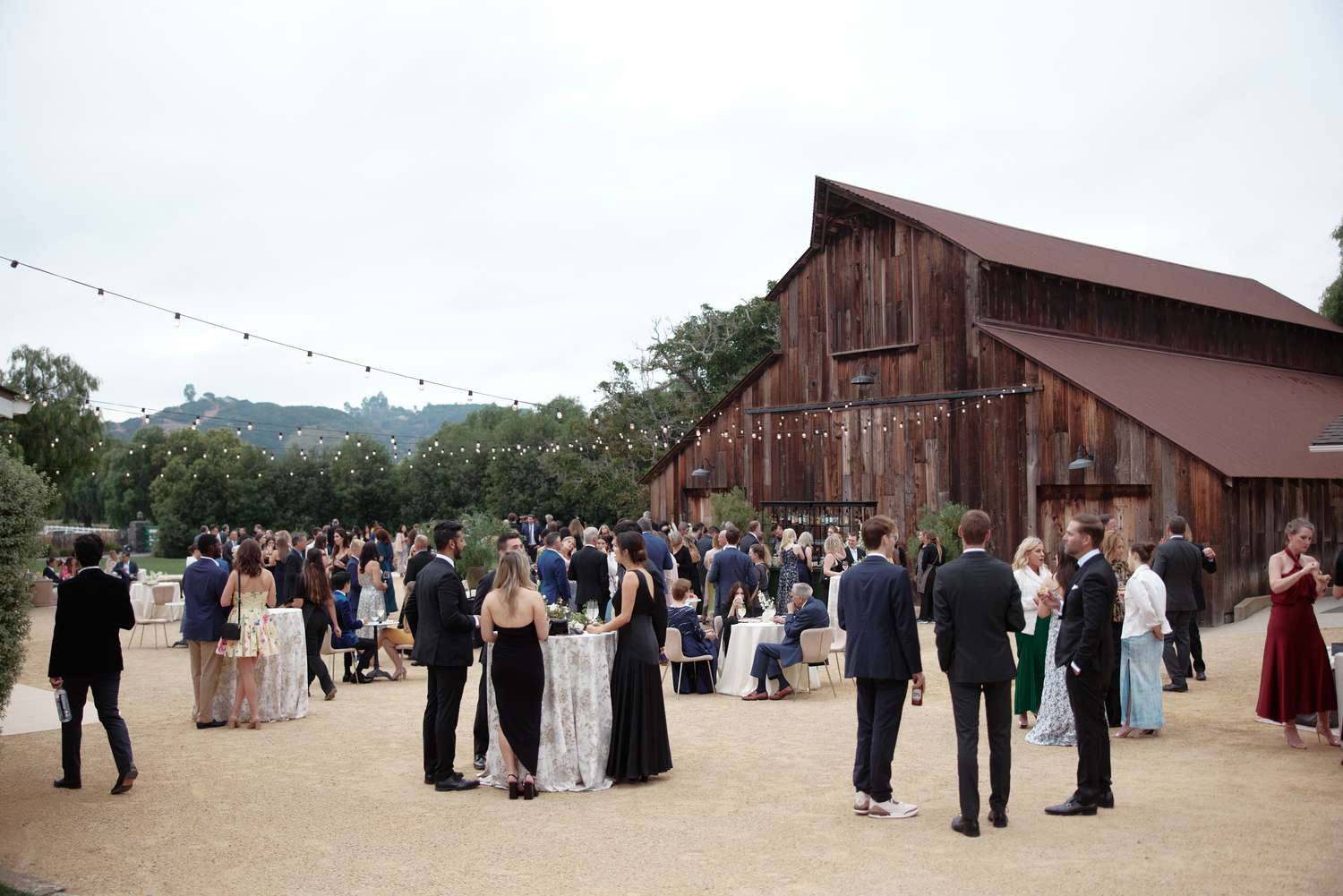 Wedding Guests in Formal Attire Having Drinks In Front of Wooden Barn Venue