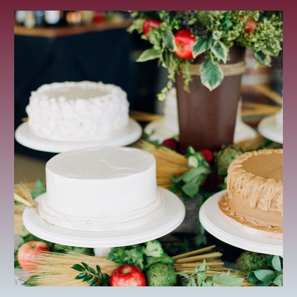 Three cakes on a cake table with potted greenery, apples, and straw