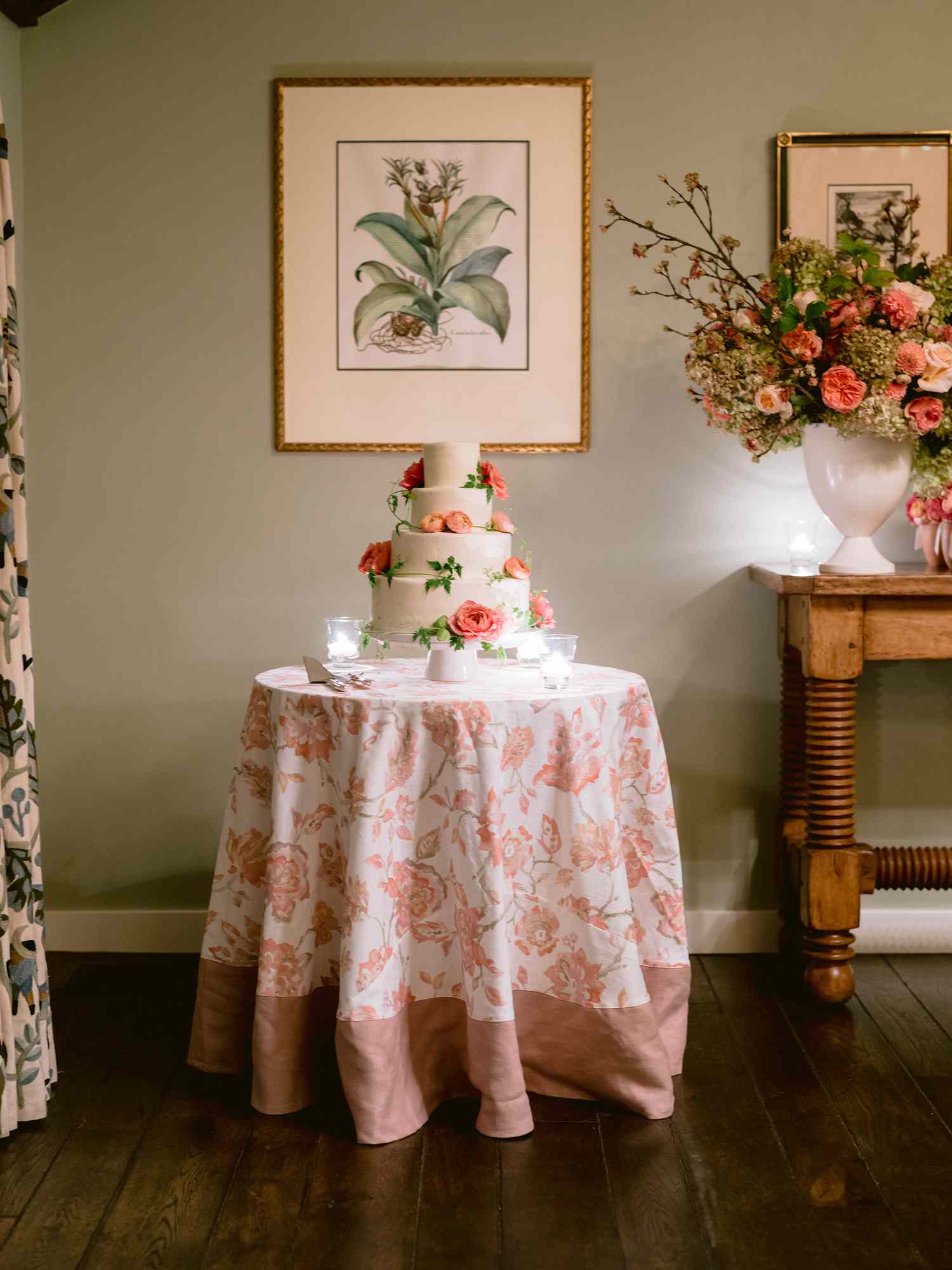 white wedding cake with flower decorations on a small round table with a flower table cloth