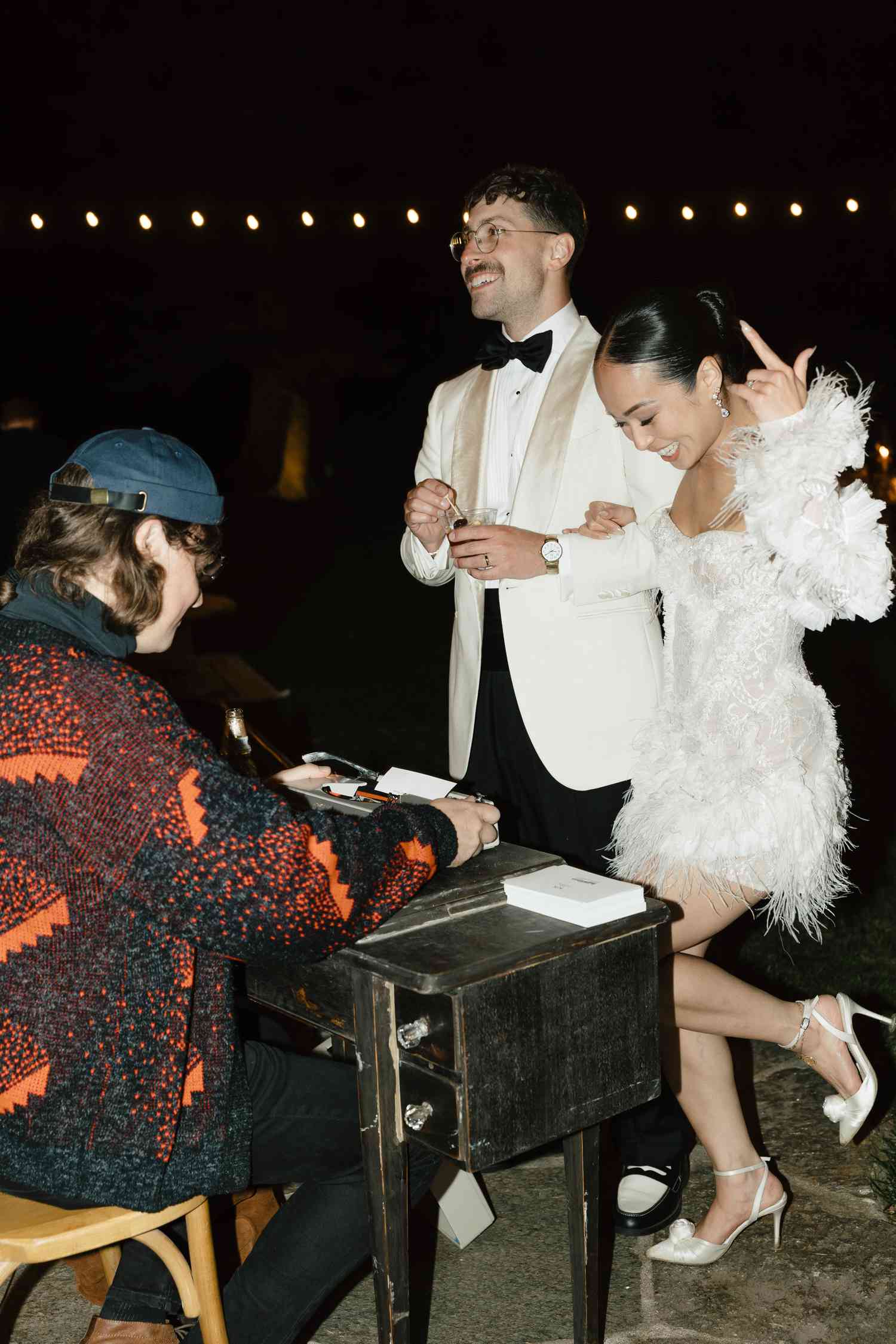 Koko lwasaki in White Mini Wedding Dress With Detached Sleeves and Kiki Nyemchek in White Tuxedo Dancing in Front of Wedding Haiku Writer