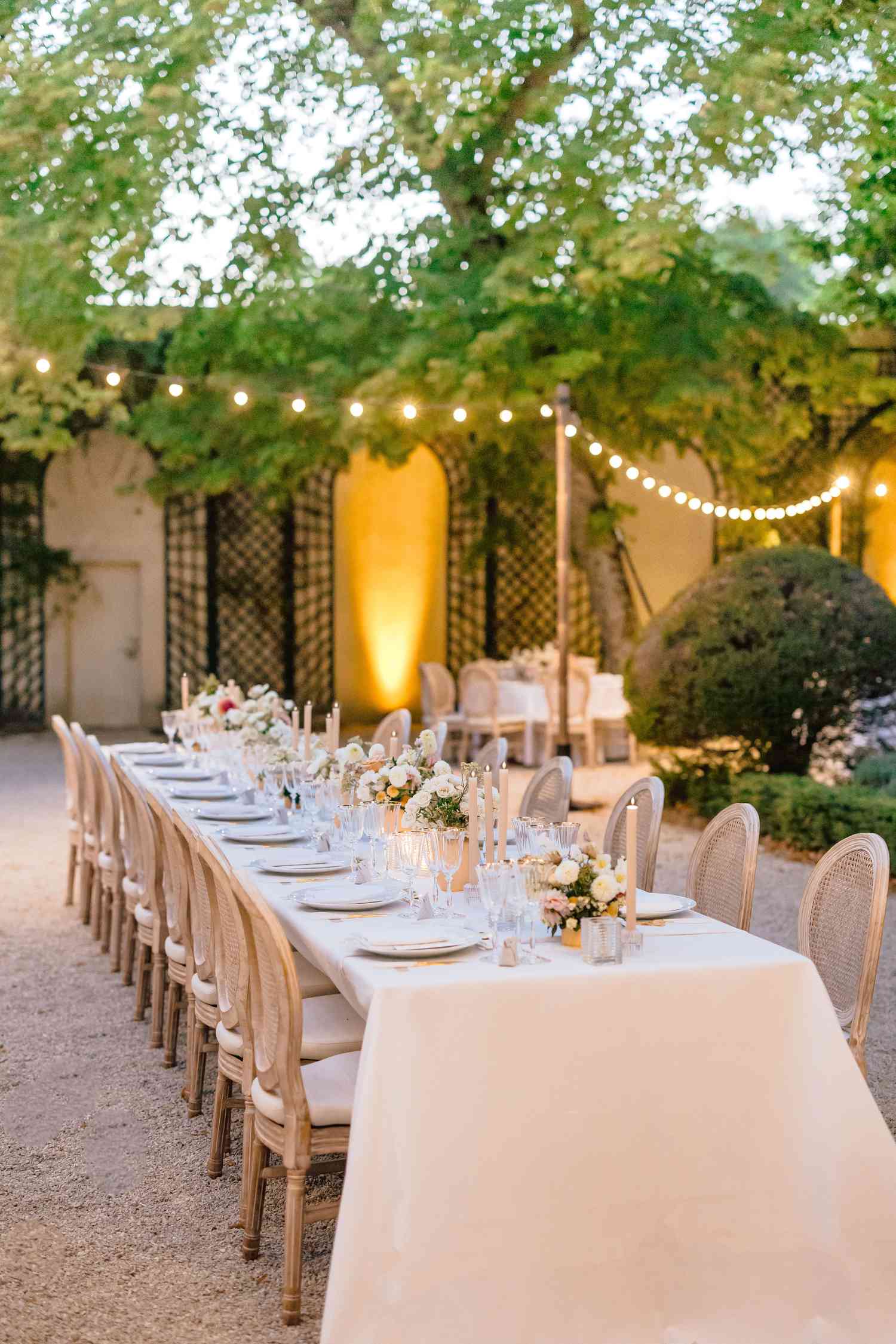 table with white table clothe and tan chairs under fairy lights