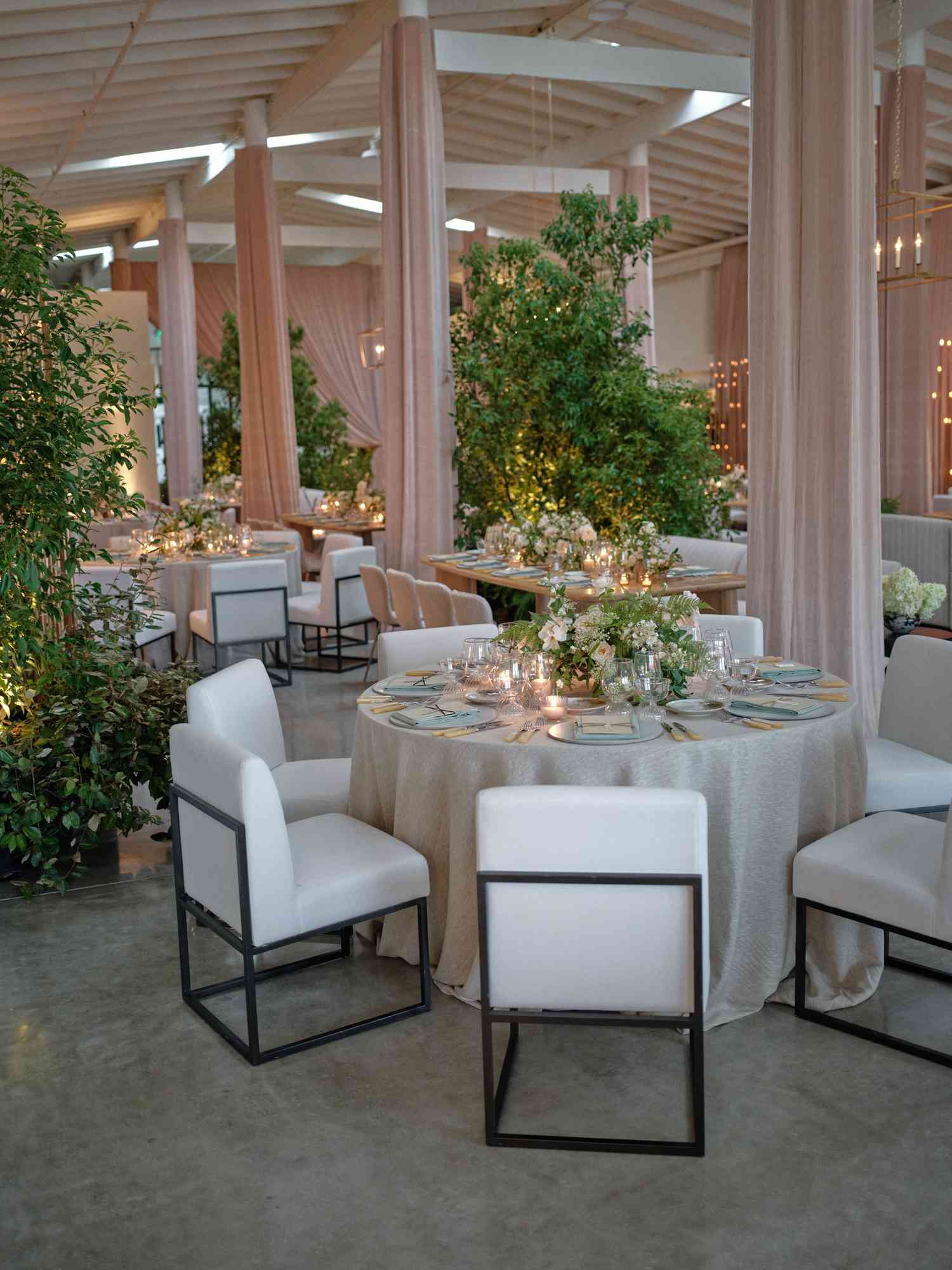Reception Tables With White Chairs and White Flower, Plant, and Candle Decor By Nude Curtains